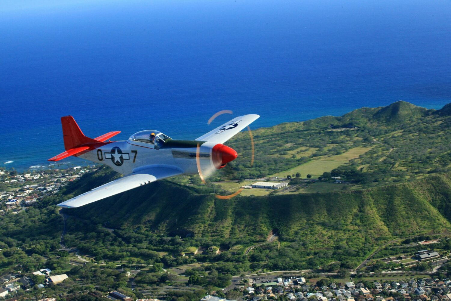 P-51 Mustang flying along a coast.  Green plateau next to a beautiful blue body of water.