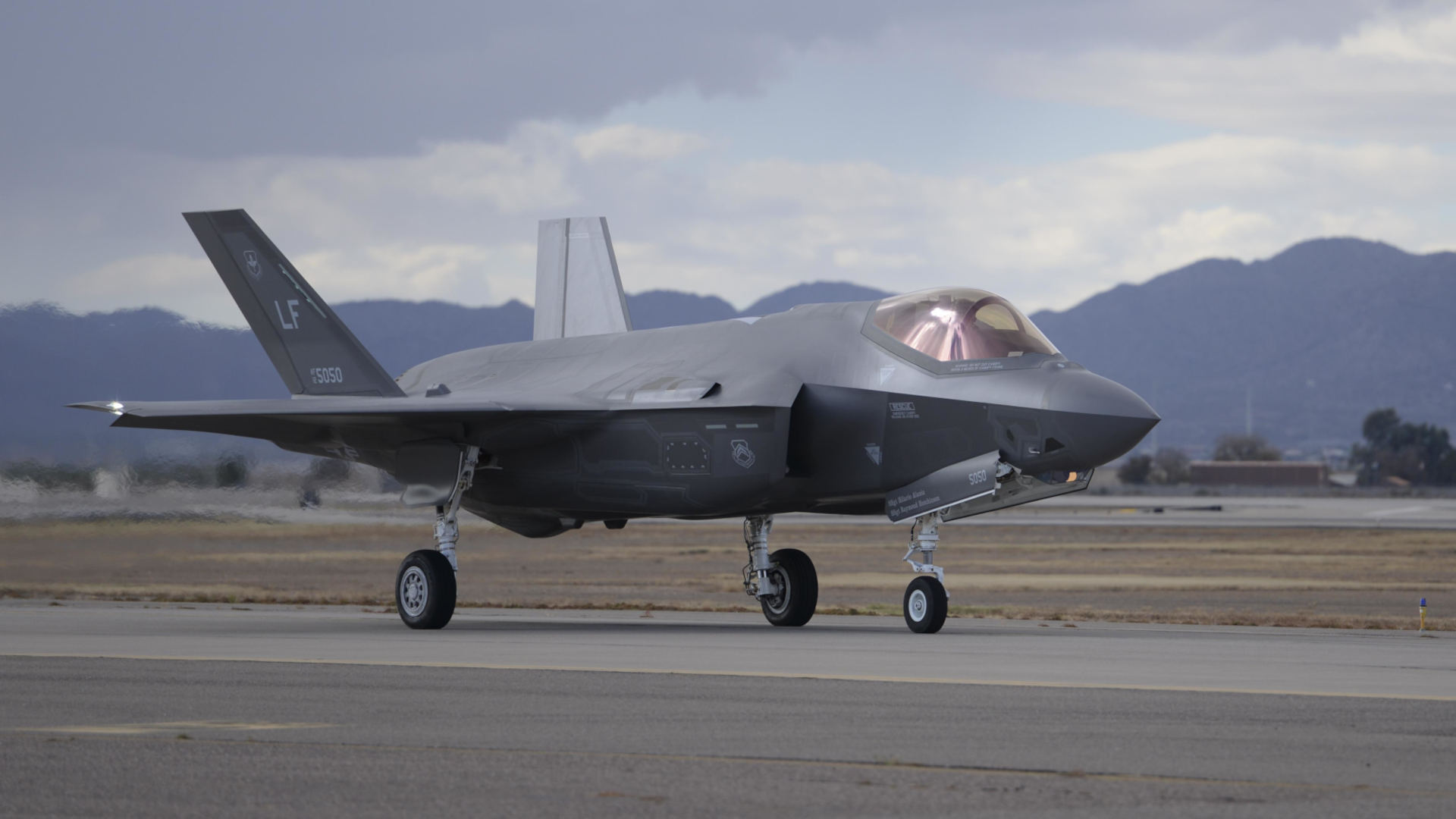 U.S. Air Force F-35 Lightning II stealth fighter taxiing on a runway, shown in profile with landing gear deployed and mountains visible in the background.
