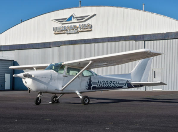 White Cessna 172 aircraft N308SU parked on pavement in front of a hangar with Hillsboro Aero signage.
