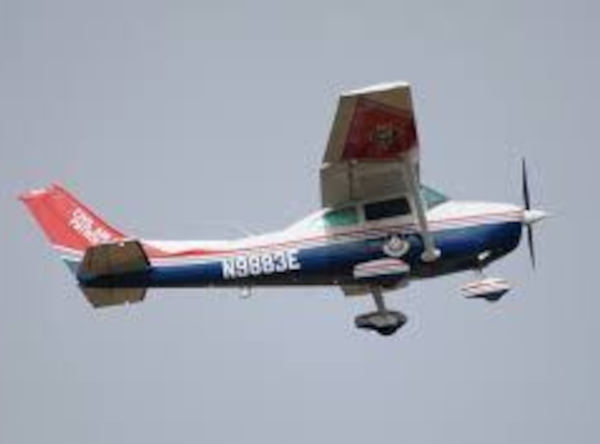 Red, white, and blue Cessna 172 N9883E flying against a clear sky with fixed landing gear visible.