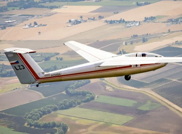 White L-23 glider N256BA soaring above patchwork farmland with fields and rural roads visible below.