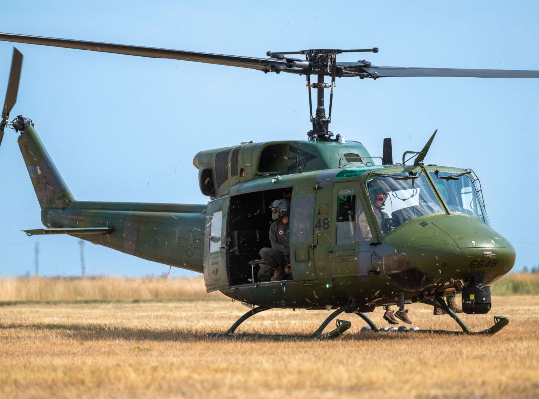 U.S. Air Force Bell UH-1 Huey helicopter hovering just above a grassy field, with crew members visible inside the open side door during a low-altitude operation.