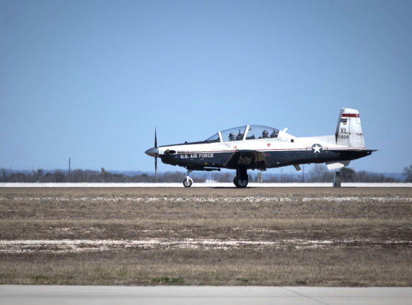 U.S. Air Force T-6 Texan II aircraft taxiing on a runway with clear sky and grassy airfield surroundings.