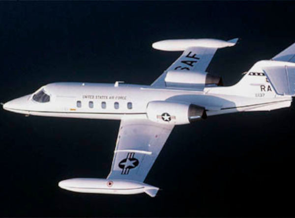 Learjet C-21 military aircraft in flight, painted white with U.S. Air Force markings, twin rear-mounted engines and swept wings, set against a dark sky background.