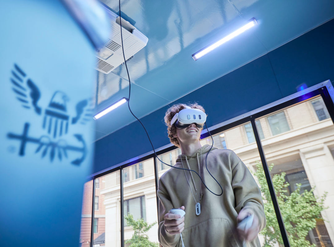A young adult uses a virtual reality headset and handheld controllers inside the U.S. Navy’s “Forged by the Sea” mobile experience.