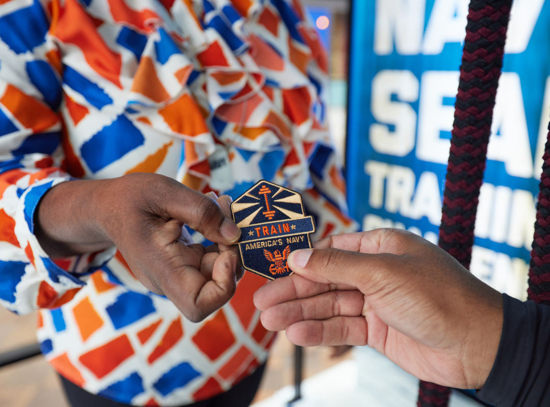 A Navy representative hands a visitor an embroidered “Train Like America’s Navy” patch.