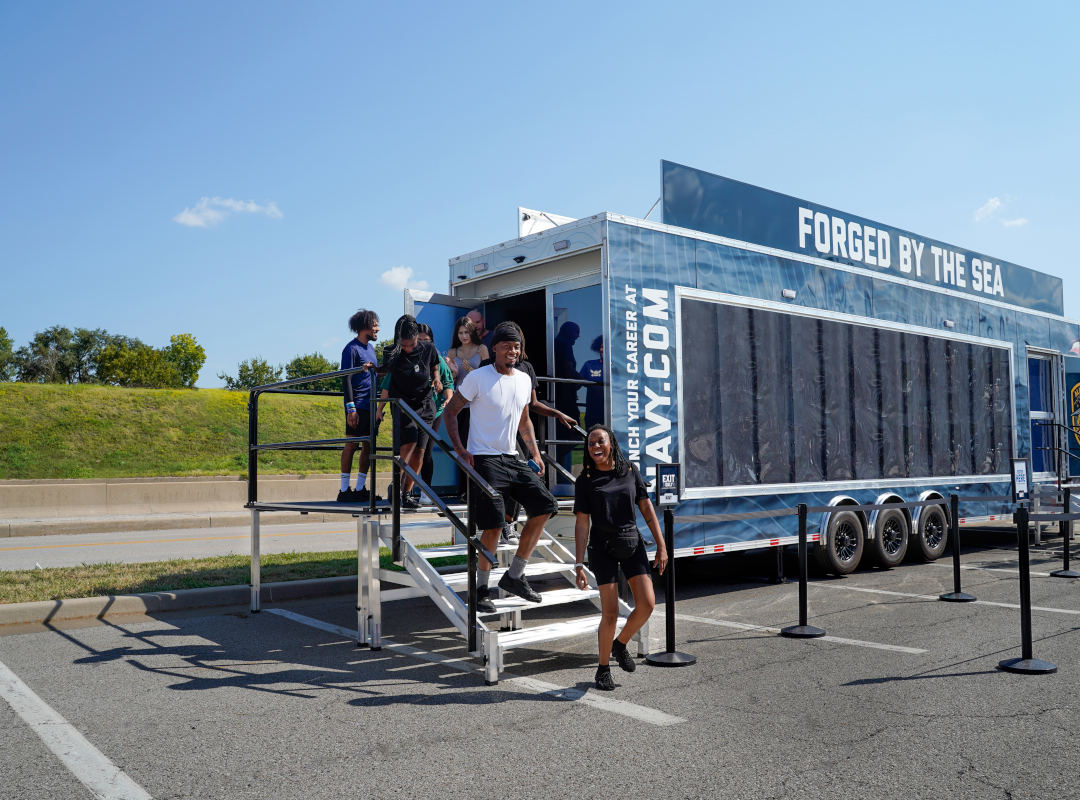 Visitors exit the U.S. Navy’s “Forged by the Sea” mobile experience trailer by an outdoor staircase.